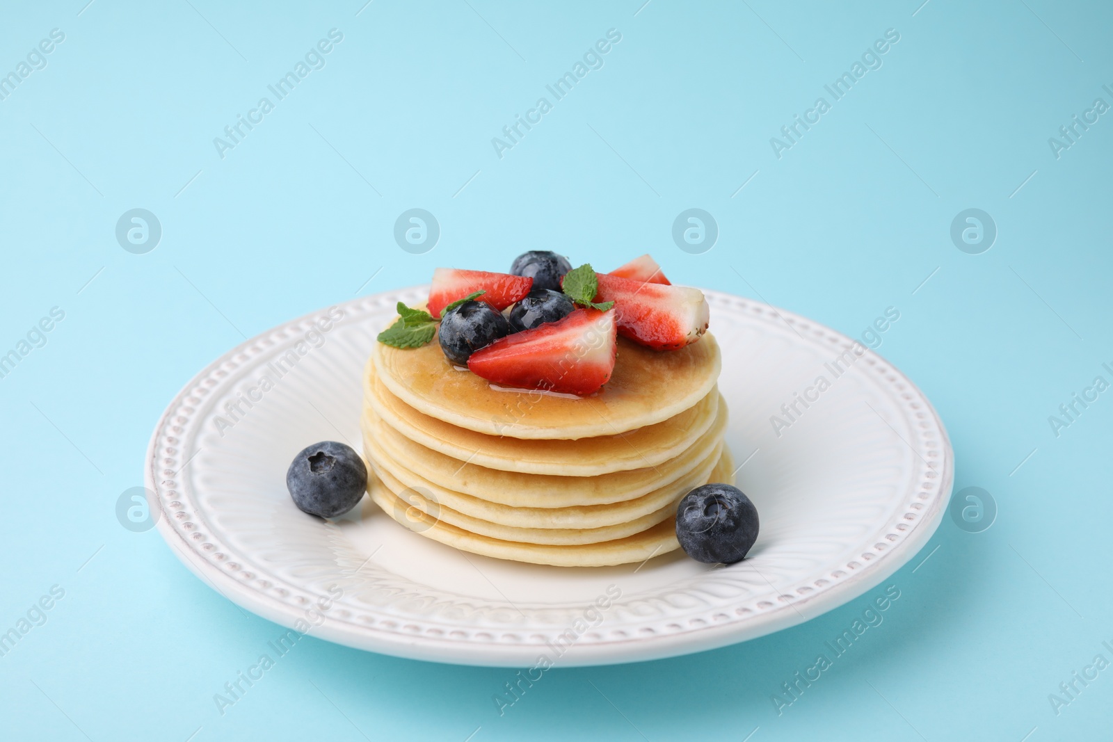 Photo of Delicious pancakes with strawberries, blueberries and mint on light blue background