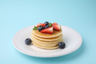 Photo of Delicious pancakes with strawberries, blueberries and mint on light blue background