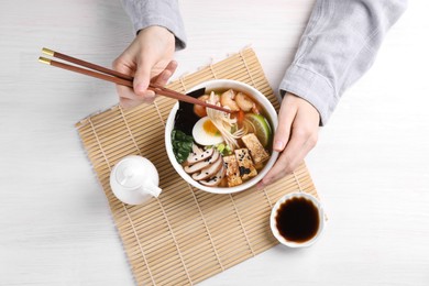 Photo of Woman eating delicious ramen with chopsticks at white table, top view. Noodle soup