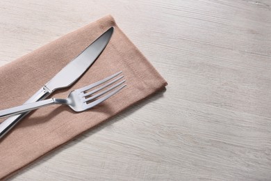 Photo of Shiny fork, knife and napkin on white wooden table, closeup. Space for text