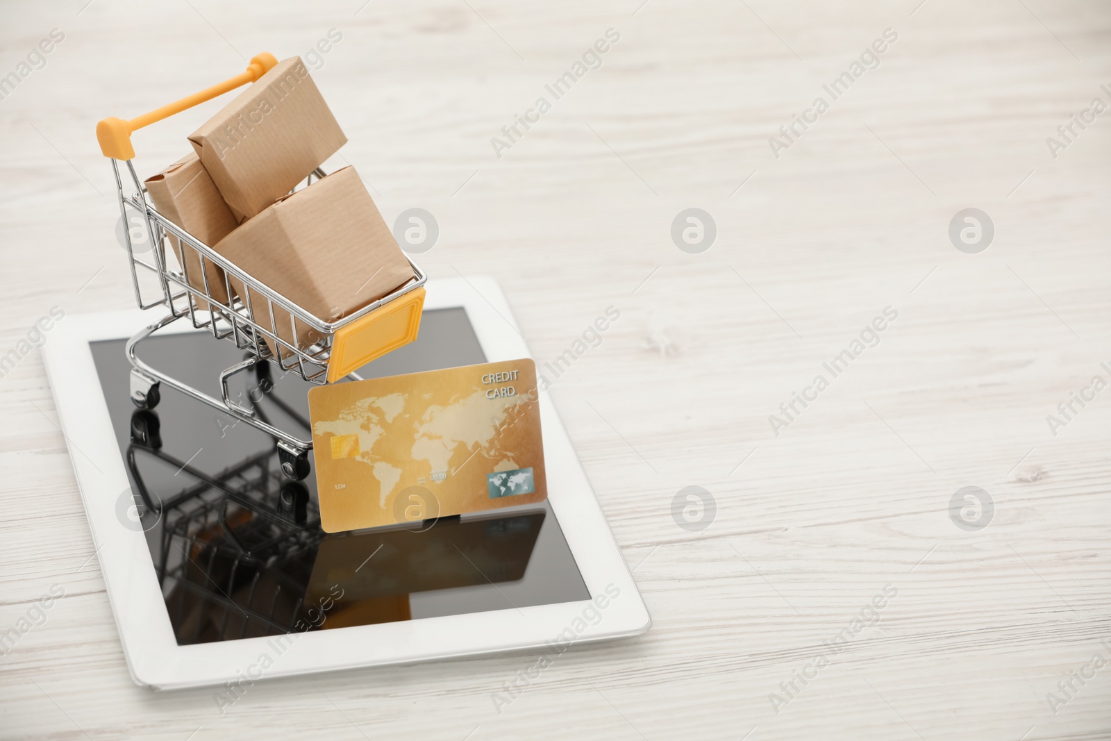 Photo of Online payment concept. Small shopping cart with bank card, boxes and tablet on white table, space for text