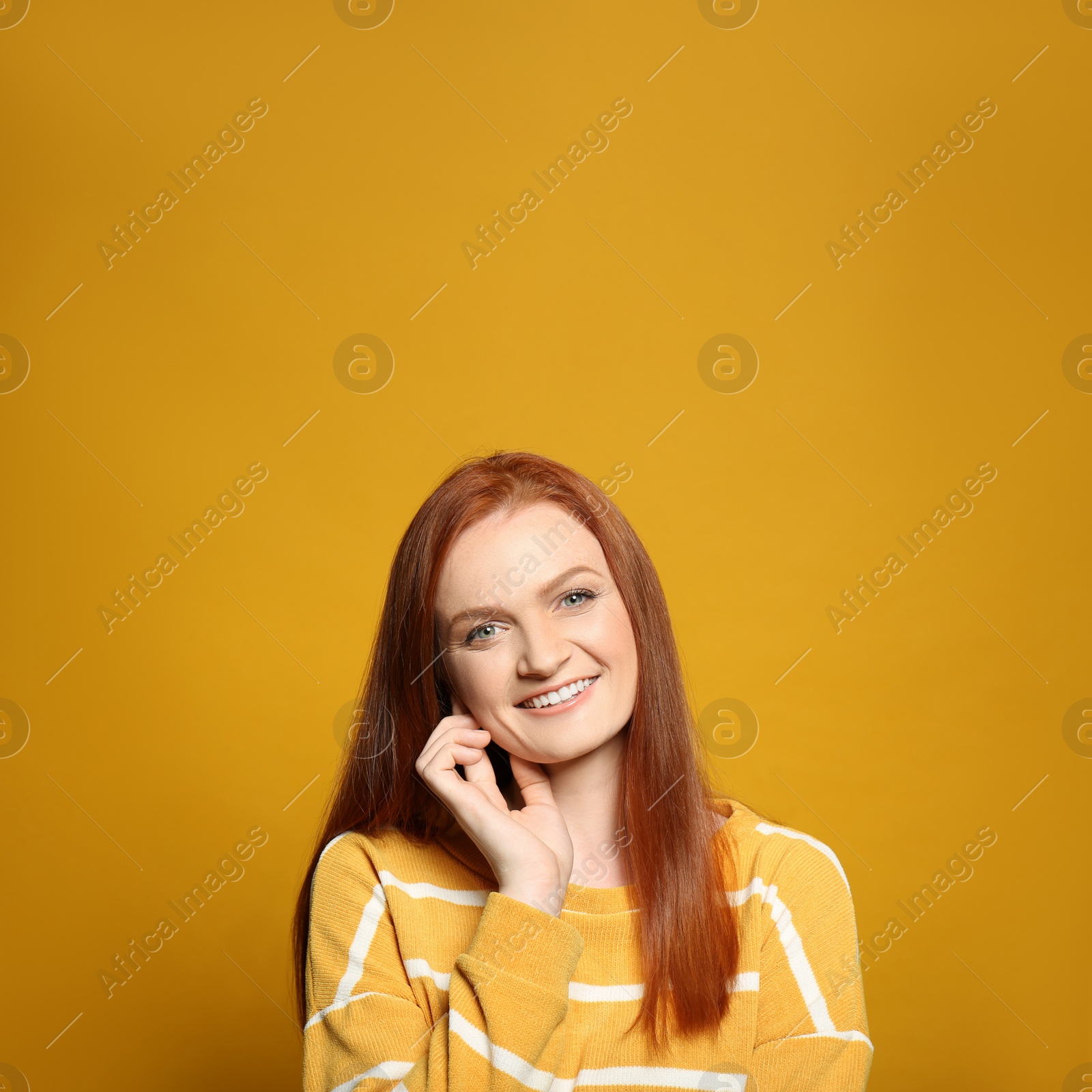 Photo of Candid portrait of happy young woman with charming smile and gorgeous red hair on yellow background