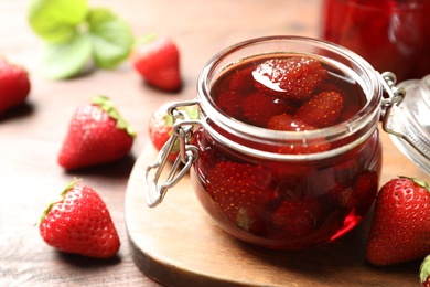 Photo of Delicious pickled strawberry jam and fresh berries on wooden table, closeup