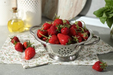 Photo of Metal colander with fresh strawberries on grey countertop in kitchen