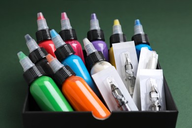 Box with colorful tattoo inks and needle cartridges on dark green background, closeup