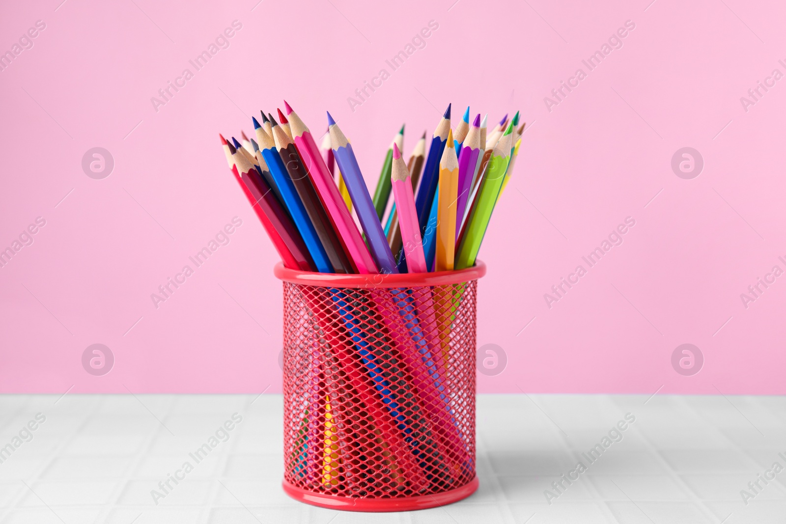 Photo of Many colorful pencils in holder on light table against pink background