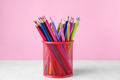 Many colorful pencils in holder on light table against pink background