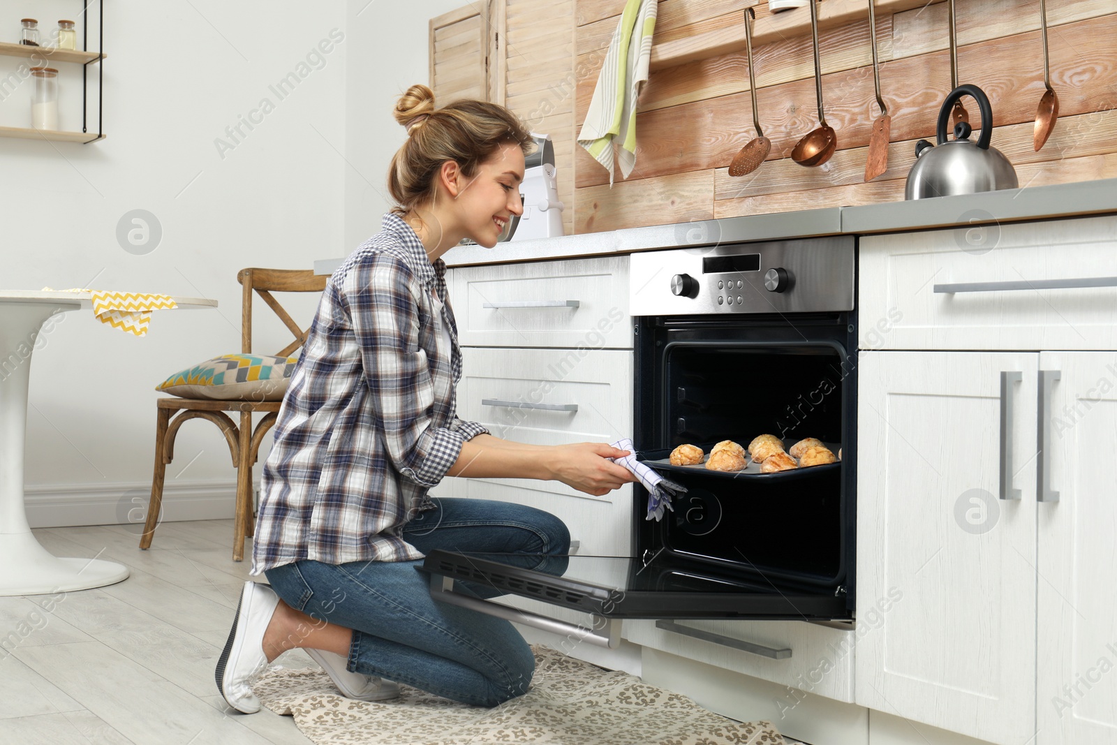 Photo of Young woman baking cookies in oven at home