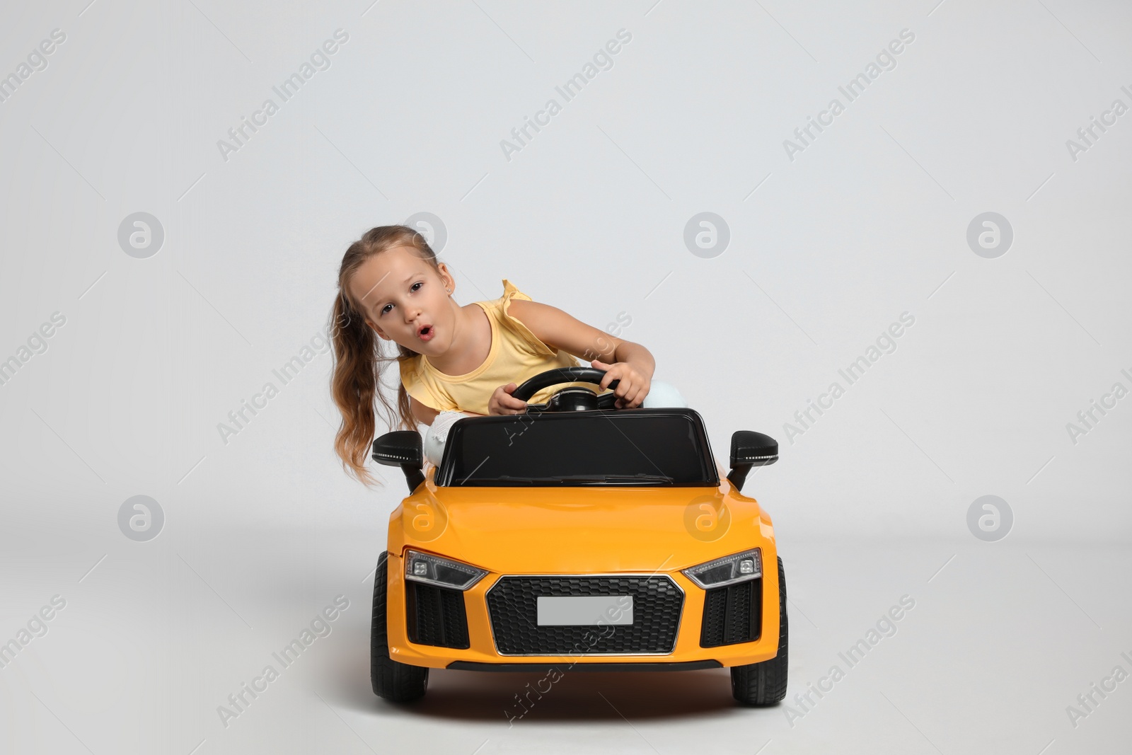 Photo of Cute little girl driving children's electric toy car on grey background