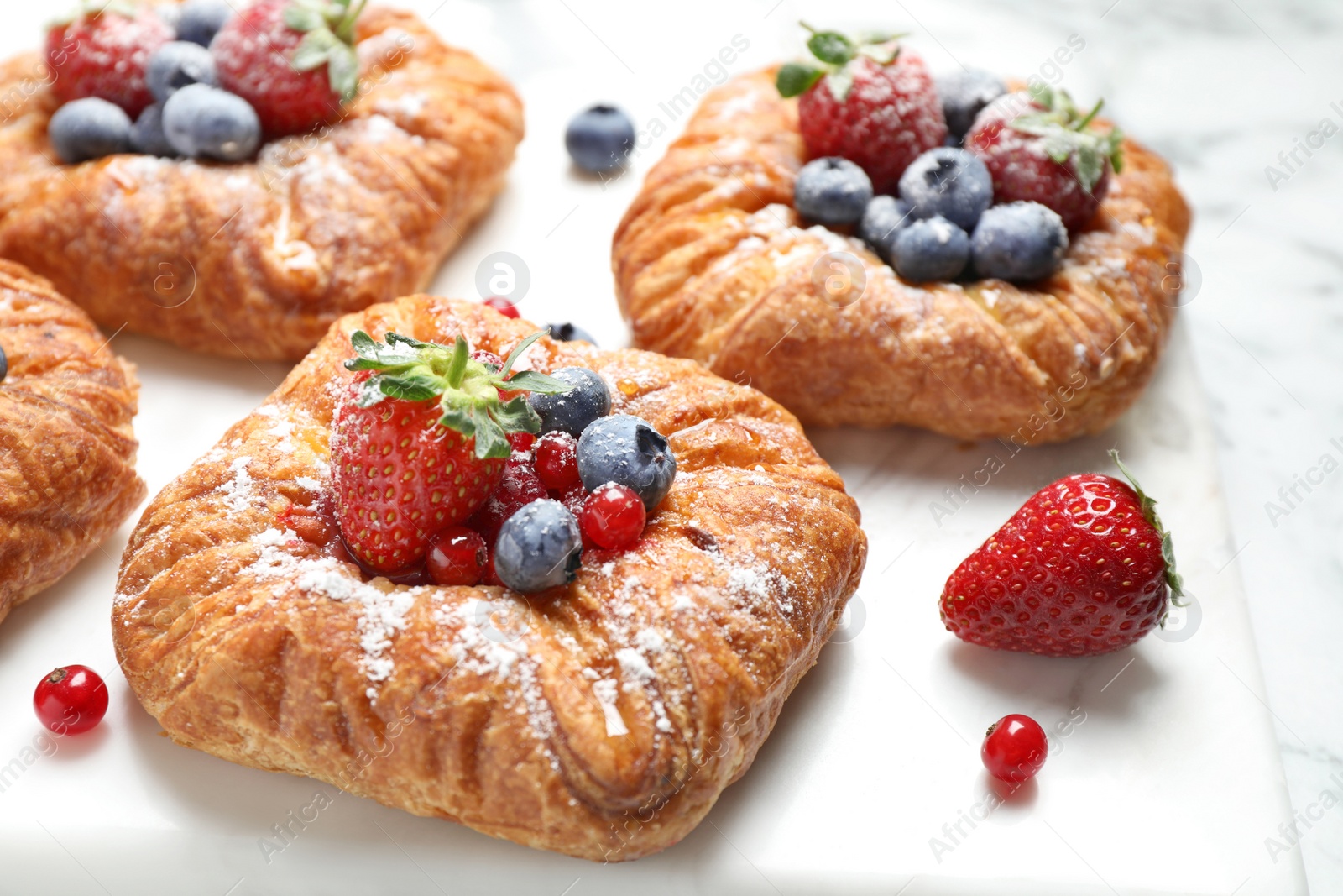 Photo of Fresh delicious puff pastry with sweet berries on white marble board, closeup