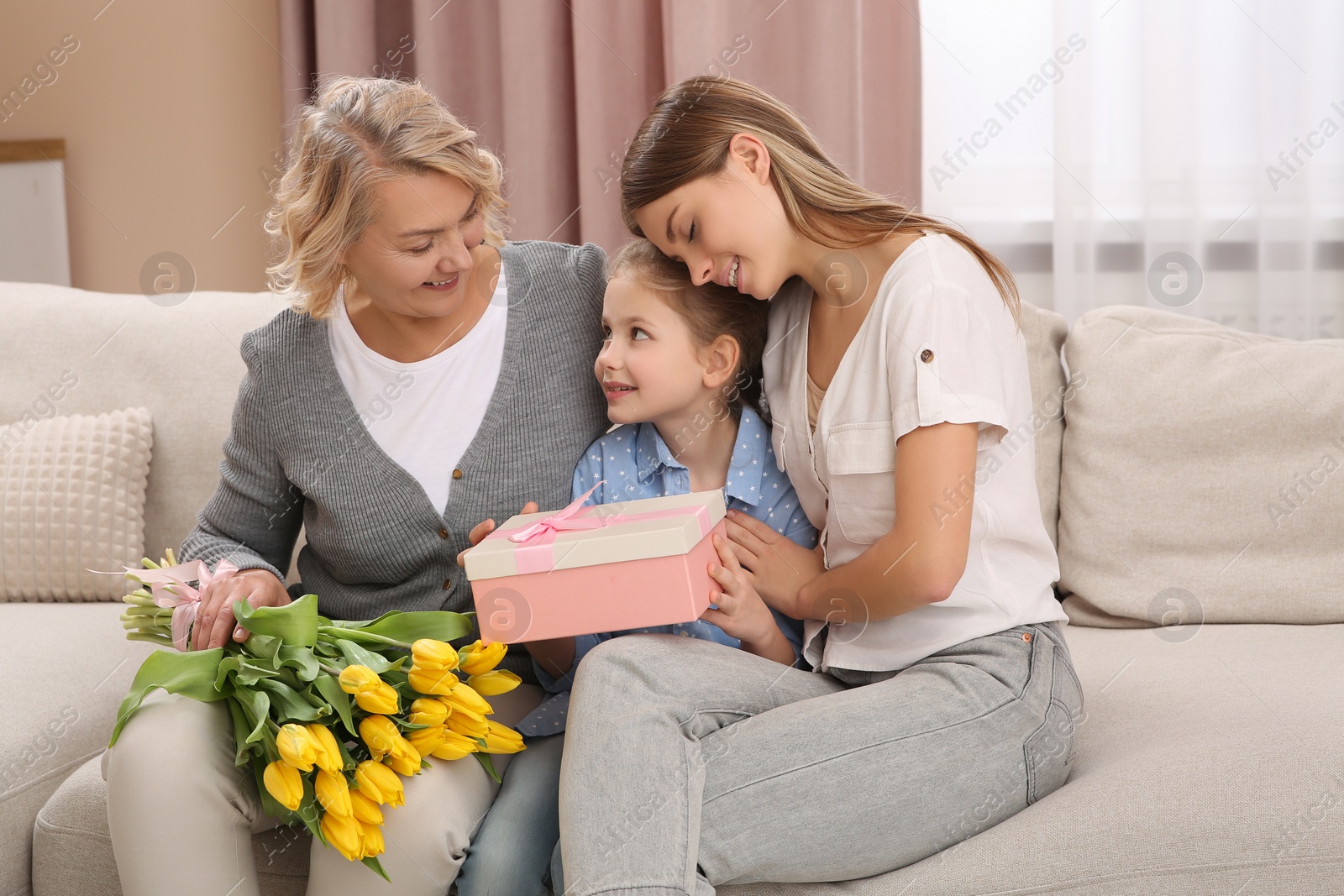 Photo of Little girl congratulating her mom and granny with flowers and gift at home. Happy Mother's Day