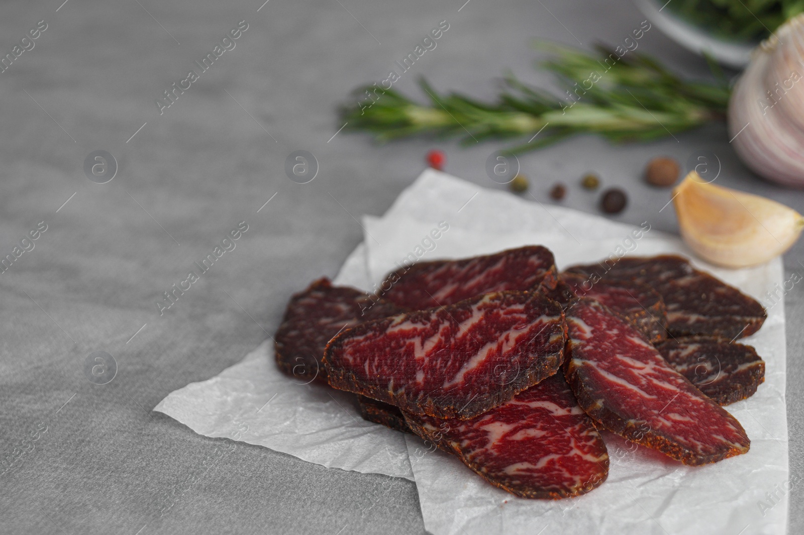 Photo of Slices of delicious beef jerky and spices on light grey table, space for text