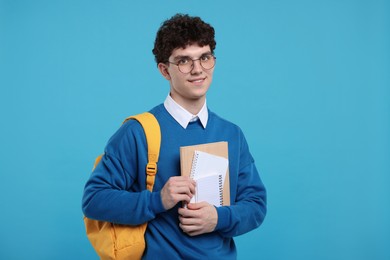 Portrait of student with backpack and notebooks on light blue background