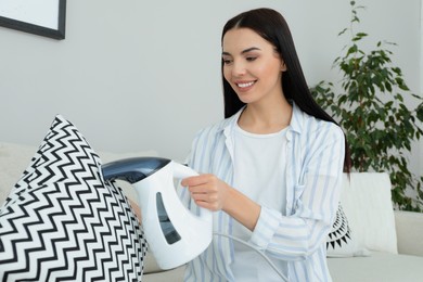 Photo of Happy woman steaming pillow in living room