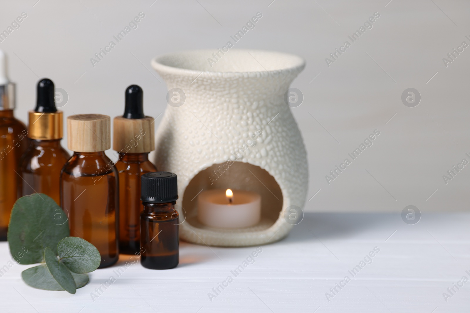 Photo of Different aromatherapy products, burning candle and eucalyptus leaves on white wooden table against light background, closeup. Space for text