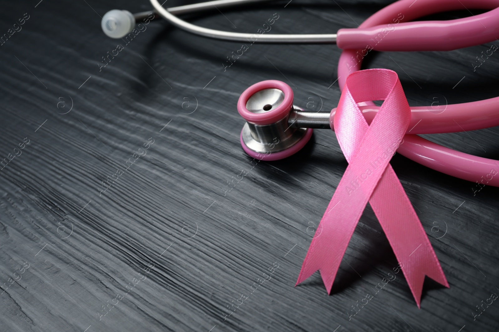 Photo of Pink ribbon and stethoscope on wooden background, space for text. Breast cancer concept