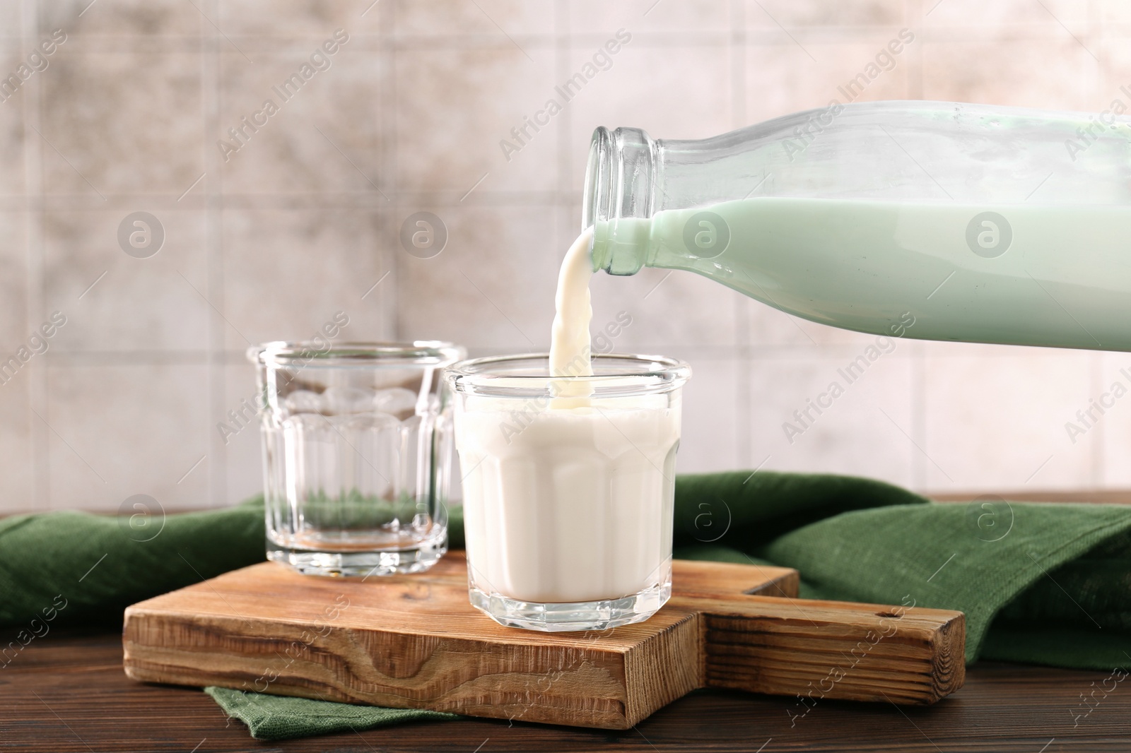 Photo of Pouring milk from bottle into glass at wooden table, closeup