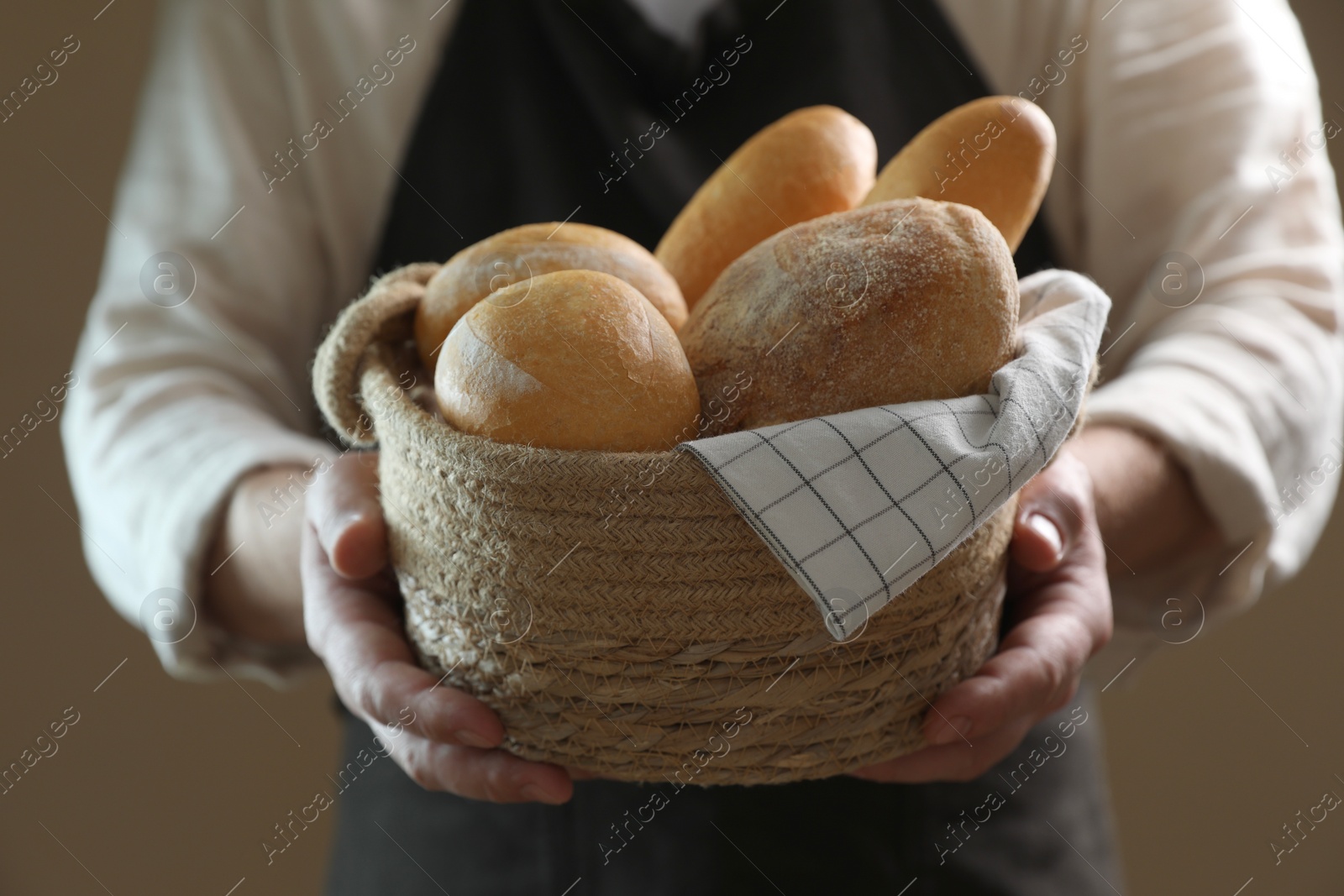 Photo of Man holding wicker basket with different types of bread on brown background, closeup