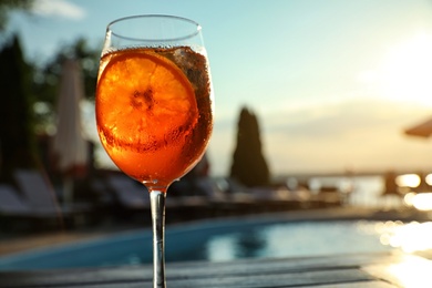 Photo of Glass of fresh summer cocktail at poolside outdoors at sunset. Space for text
