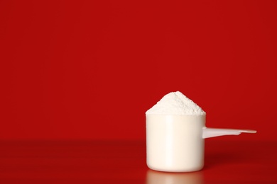 Photo of Scoop of protein powder on table against red background. Space for text