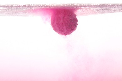 Photo of Pink bath bomb in clear water on white background