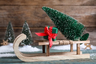 Sleigh with decorative Christmas tree and gift box on blue wooden table