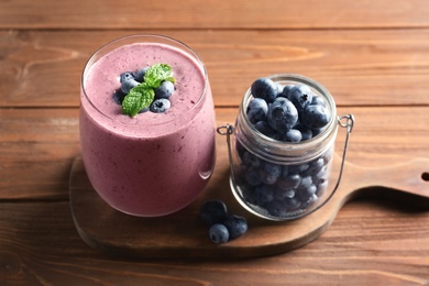 Photo of Glass of smoothie and jar with blueberries on wooden background