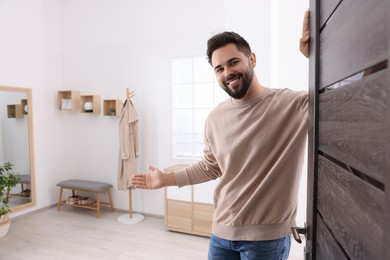 Photo of Happy man welcoming near door, space for text. Invitation to come indoors
