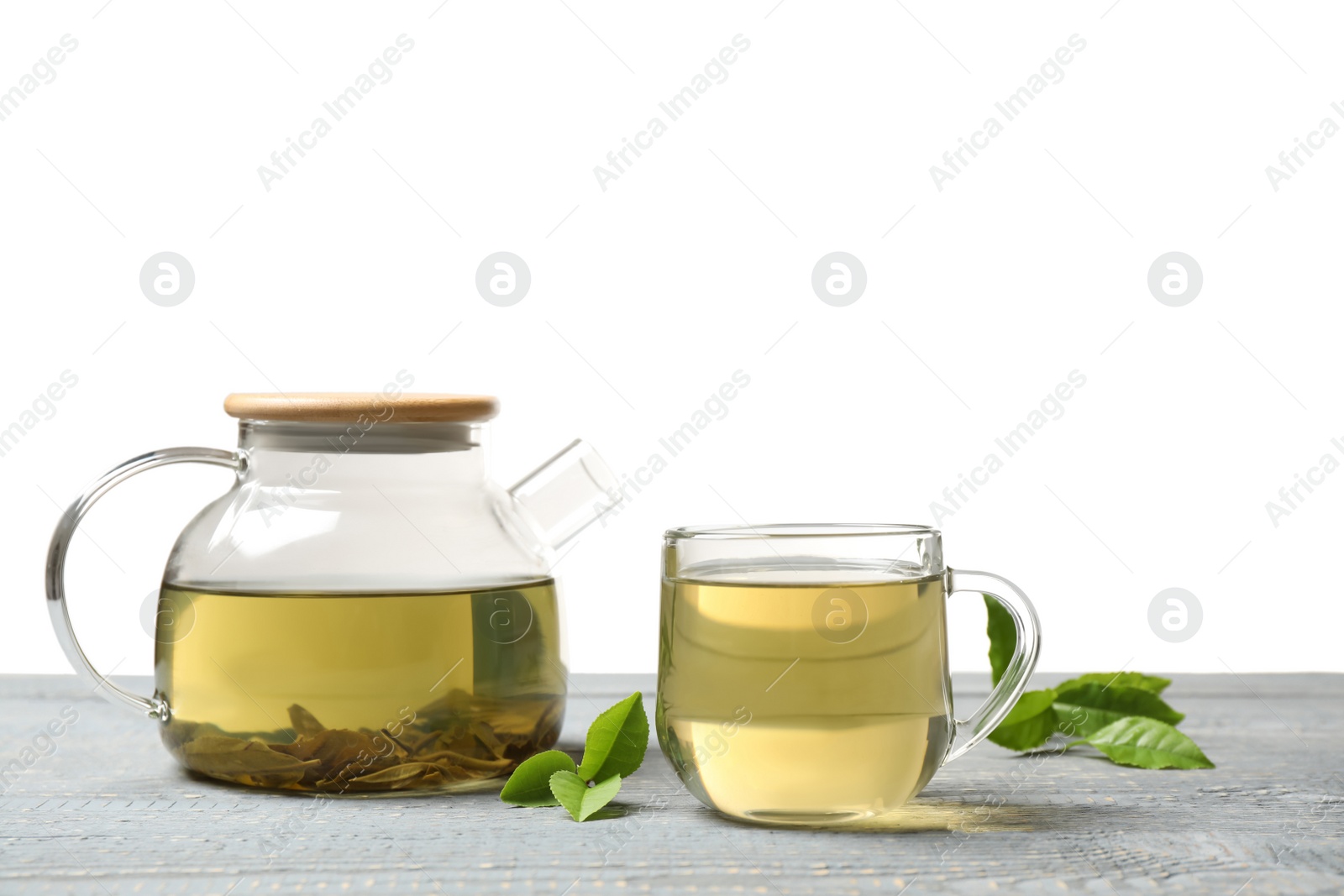 Photo of Cup of green tea, pot and leaves on grey wooden table
