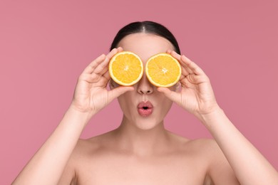 Photo of Beautiful young woman covering face with pieces of orange on pink background