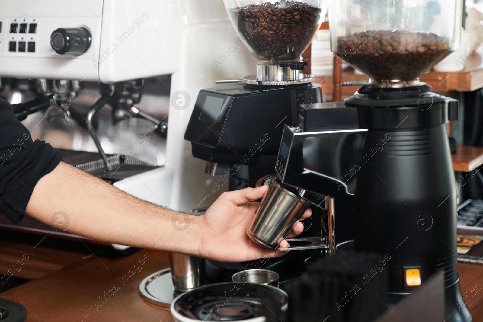 Photo of Barista with metal cup using coffee grinding machine in cafe, closeup