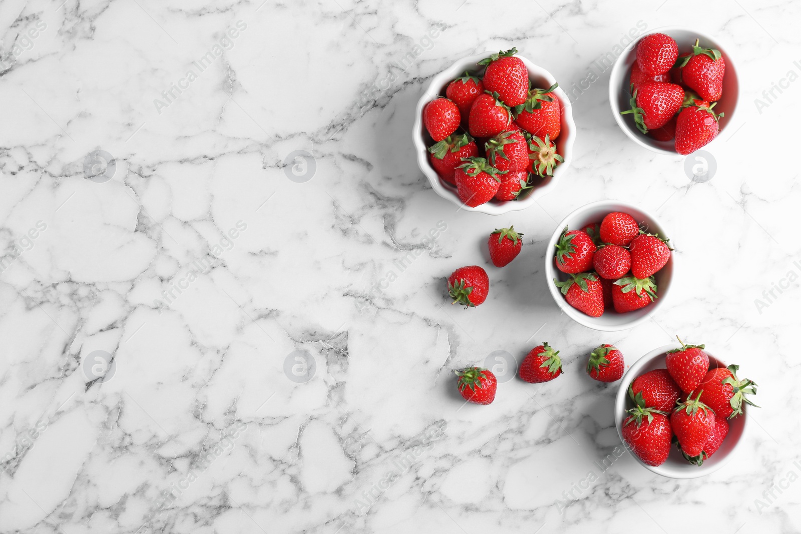 Photo of Bowls with ripe red strawberries on marble background, top view