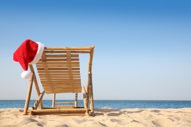 Sun lounger with Santa's hat on beach, space for text. Christmas vacation