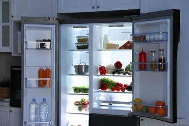 Open refrigerator full of different products in kitchen