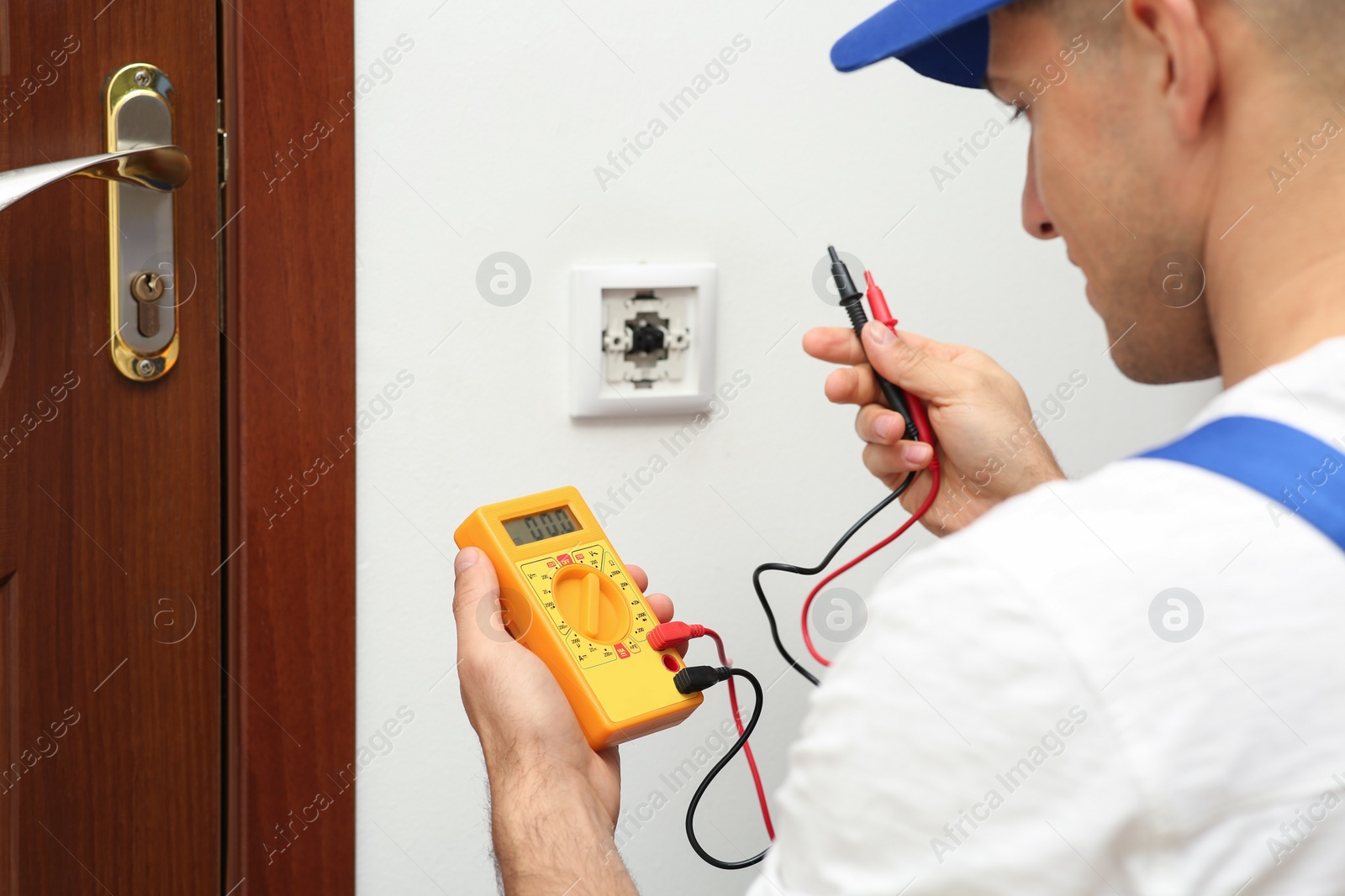 Photo of Professional electrician with voltage tester near power light switch indoors, closeup