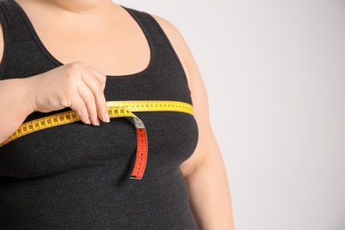 Photo of Overweight woman with measuring tape on light background