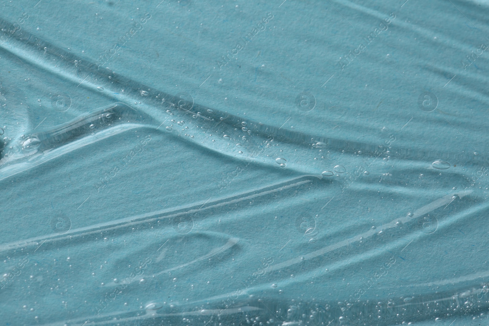 Photo of Clear cosmetic serum on light blue background, macro view