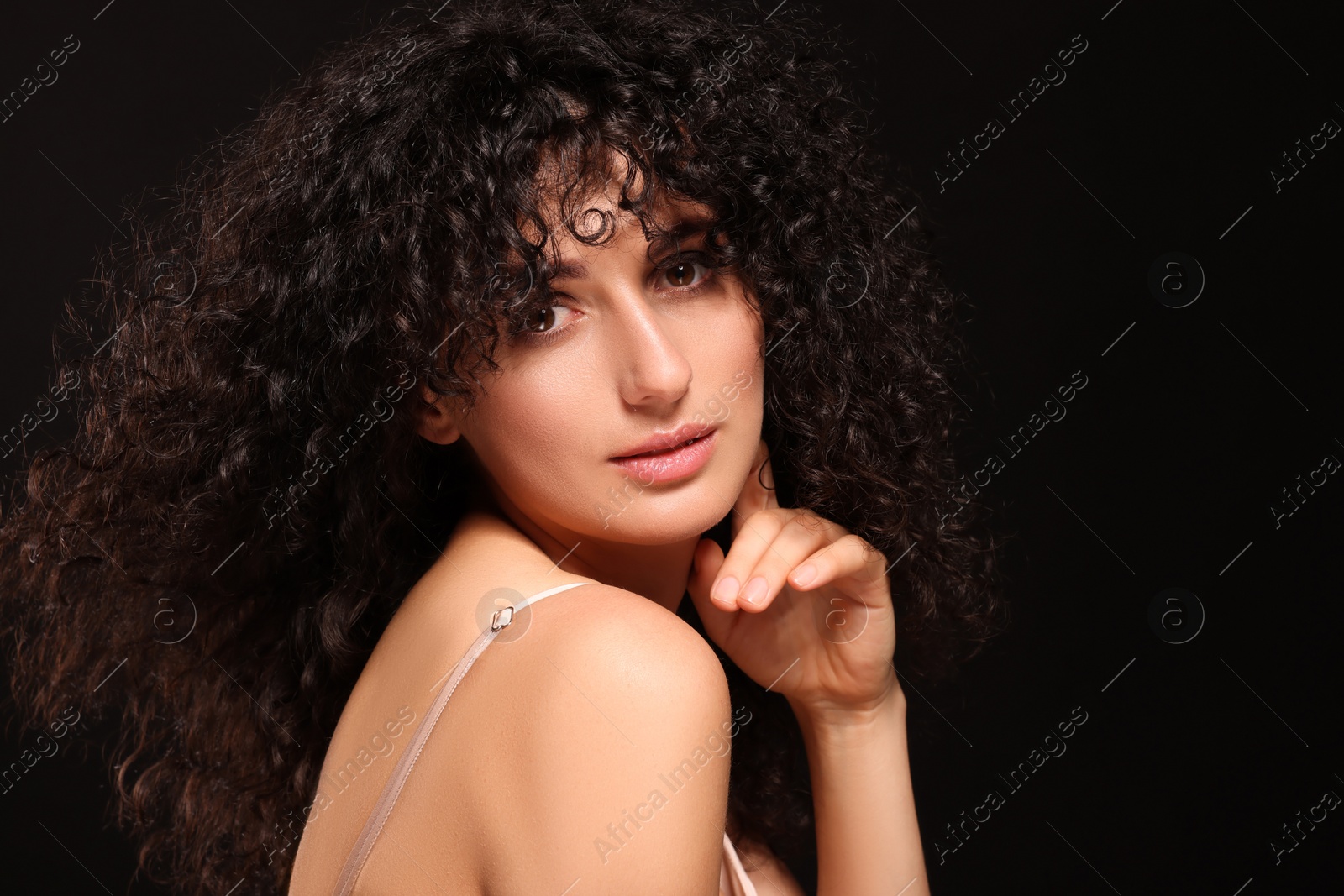 Photo of Beautiful young woman with long curly hair on black background