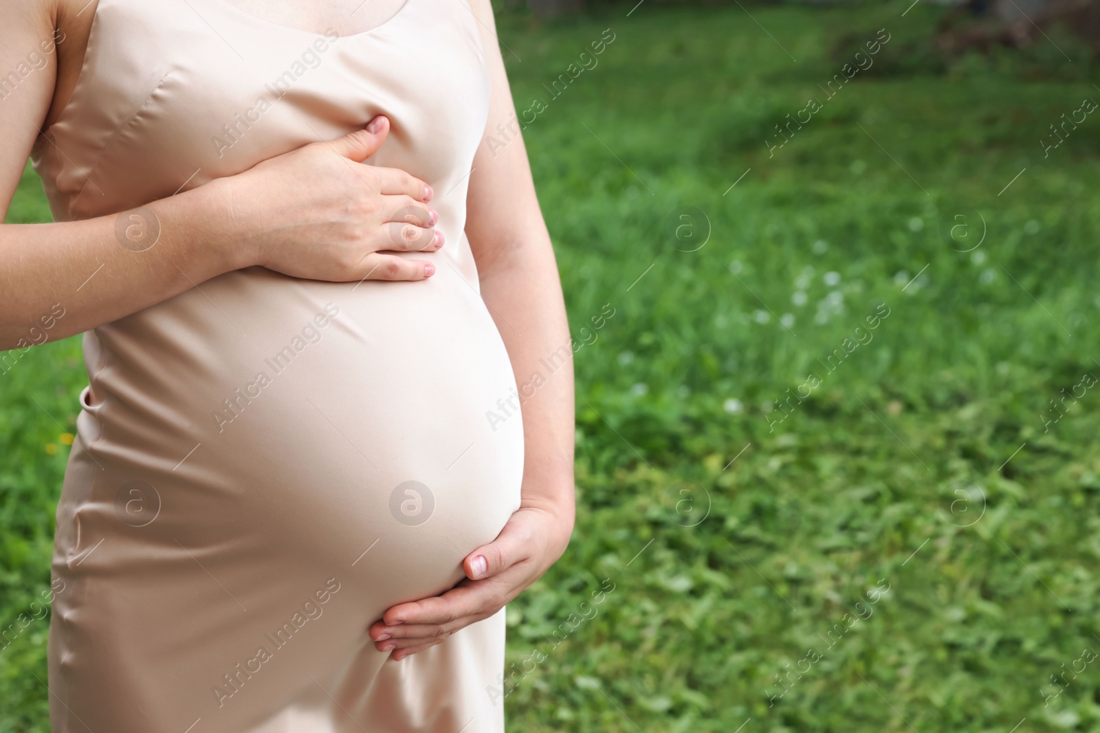 Photo of Pregnant woman touching belly on green grass, closeup. Space for text