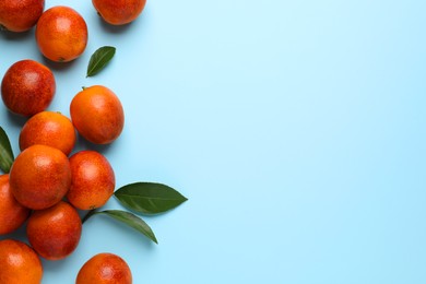 Many ripe sicilian oranges and leaves on light blue background, flat lay. Space for text