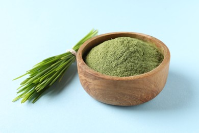 Photo of Wheat grass powder in bowl and fresh sprouts on light blue background, closeup
