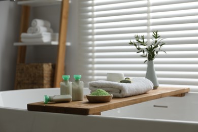 Photo of Wooden tray with spa products and green branches on bath tub in bathroom