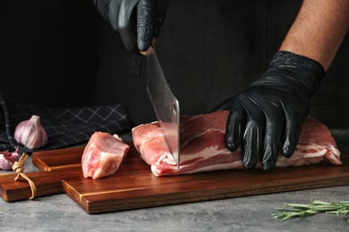 Man cutting fresh raw meat on table against dark background, closeup