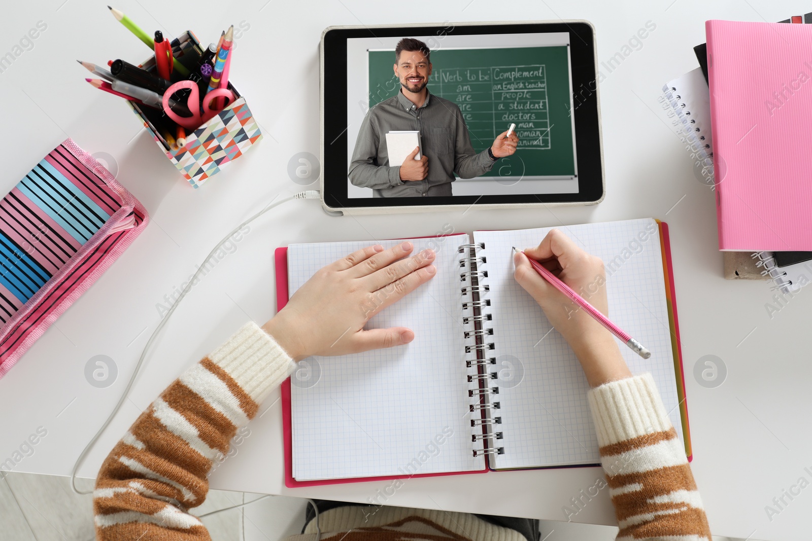 Image of E-learning. Girl taking notes during online lesson at table indoors, top view