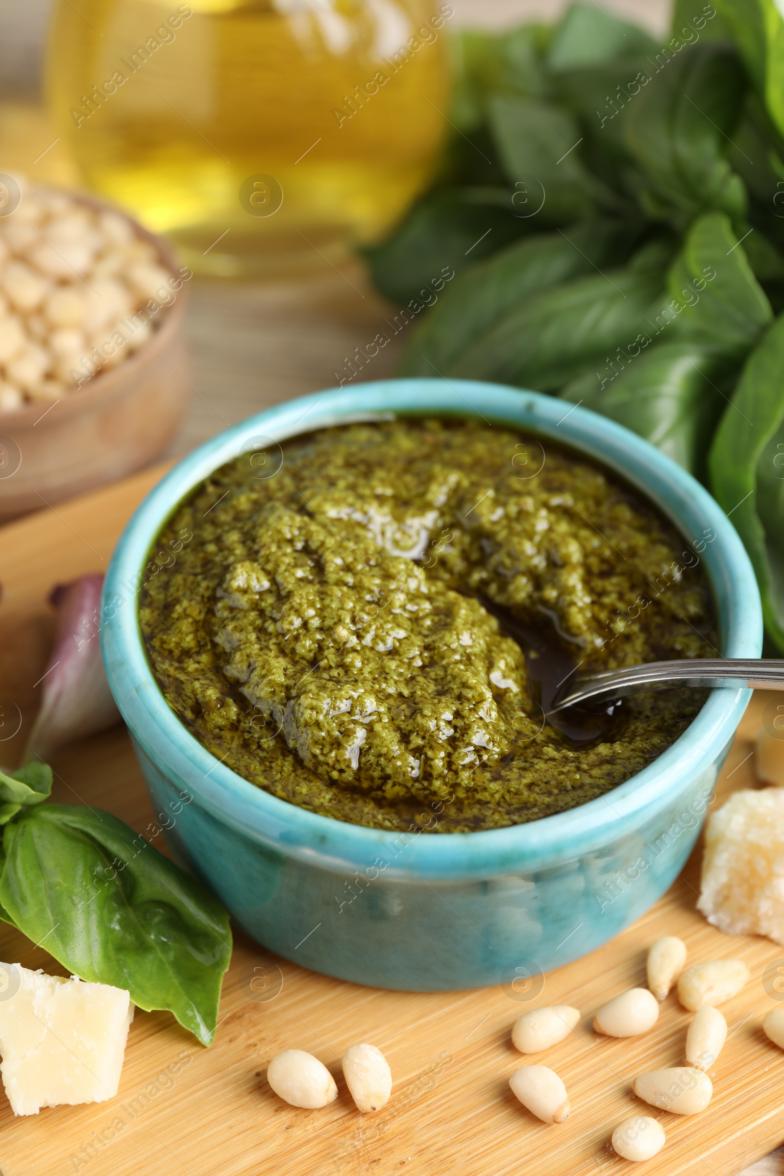 Photo of Tasty pesto sauce in bowl, basil, pine nuts and cheese on table