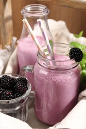 Photo of Different glassware of delicious blackberry smoothie and fresh berries on wooden background, closeup