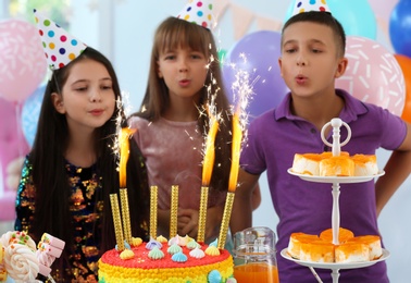 Happy children near cake with firework candles at birthday party indoors