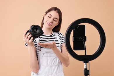 Photo of Technology blogger reviewing camera and recording video with smartphone and ring lamp on beige background
