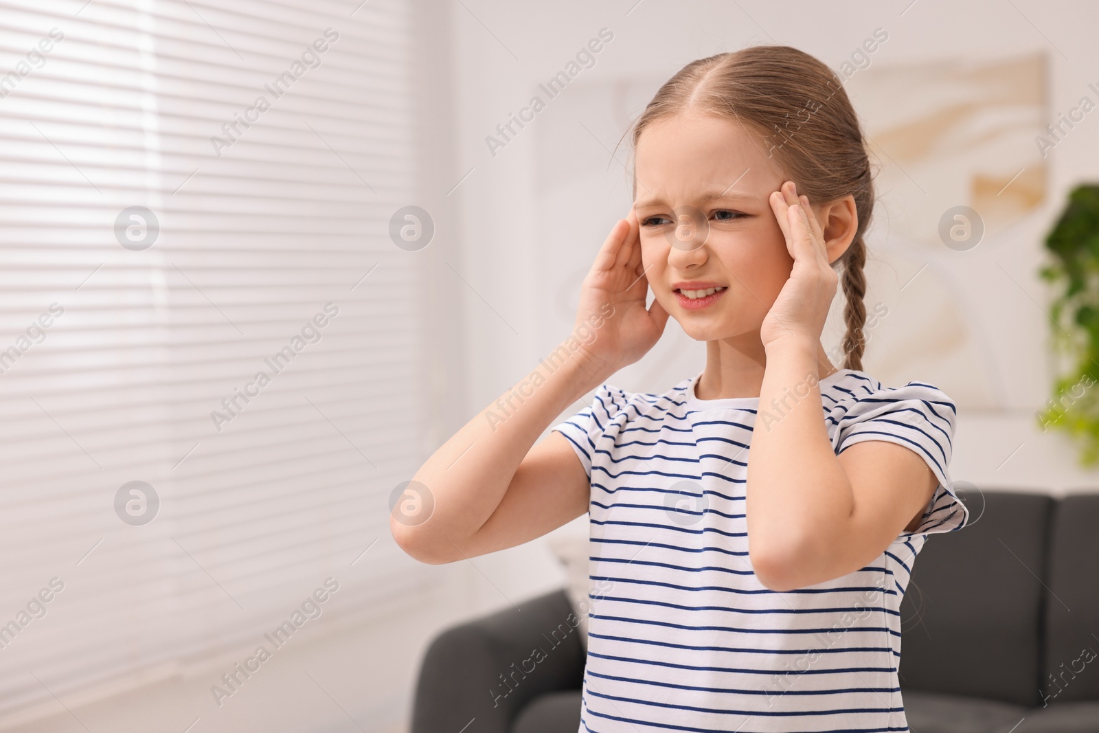 Photo of Little girl suffering from headache at home. Space for text