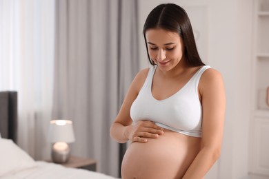 Photo of Beautiful pregnant woman wearing stylish comfortable underwear in bedroom, space for text